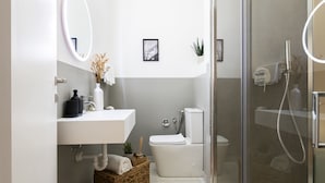 A modern bathroom with a white sink, mirror, and toilet. There is a shower area with a glass door. - Easylife-Sophisticated  with Jacuzzi in Centrale (Milano)