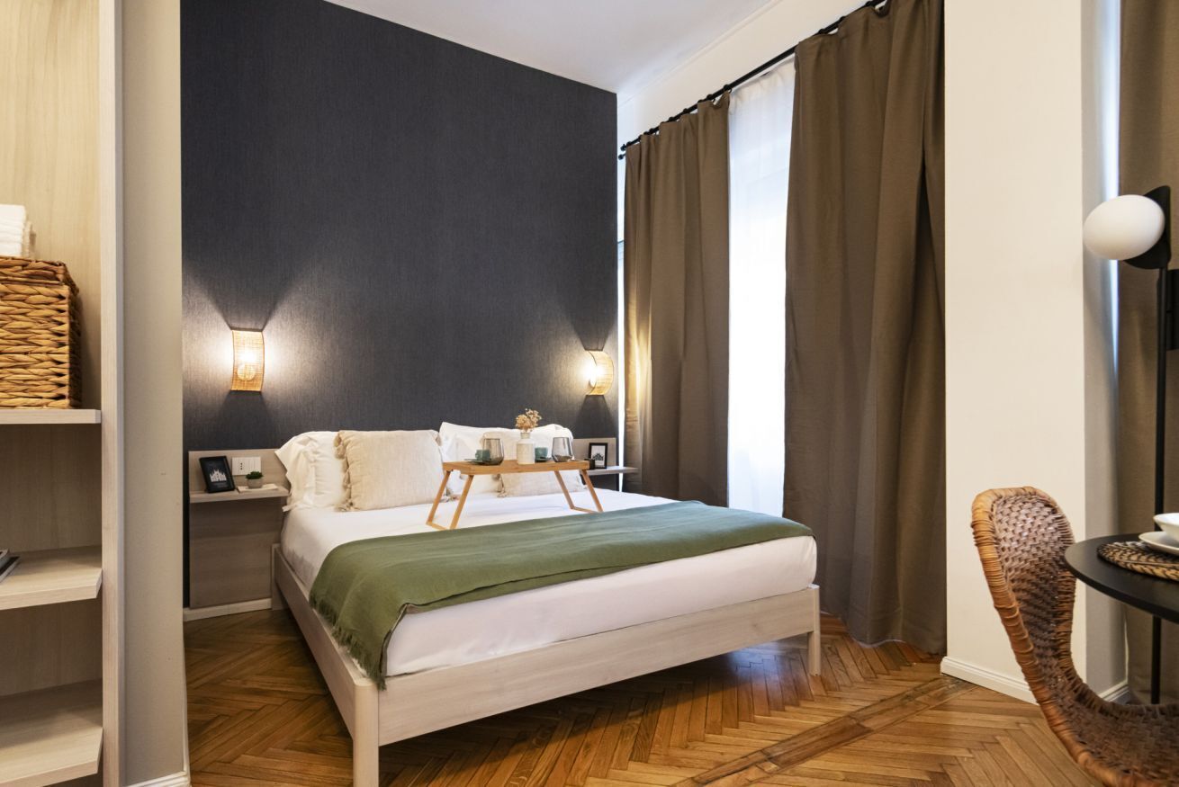 Habitación de hotel con cama, mesitas de noche, lámpara, silla y vistas al exterior.