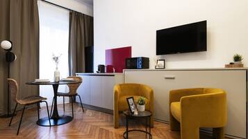 Ein modernes Wohnzimmer mit Essbereich, einem wandmontierten Flachbildfernseher und einer Küchenzeile mit roter Akzentwand.