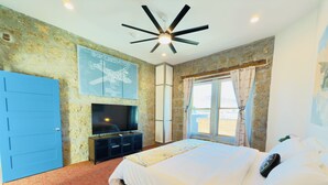 Un dormitorio con cama, televisor, ventilador de techo y ventana con cortinas.