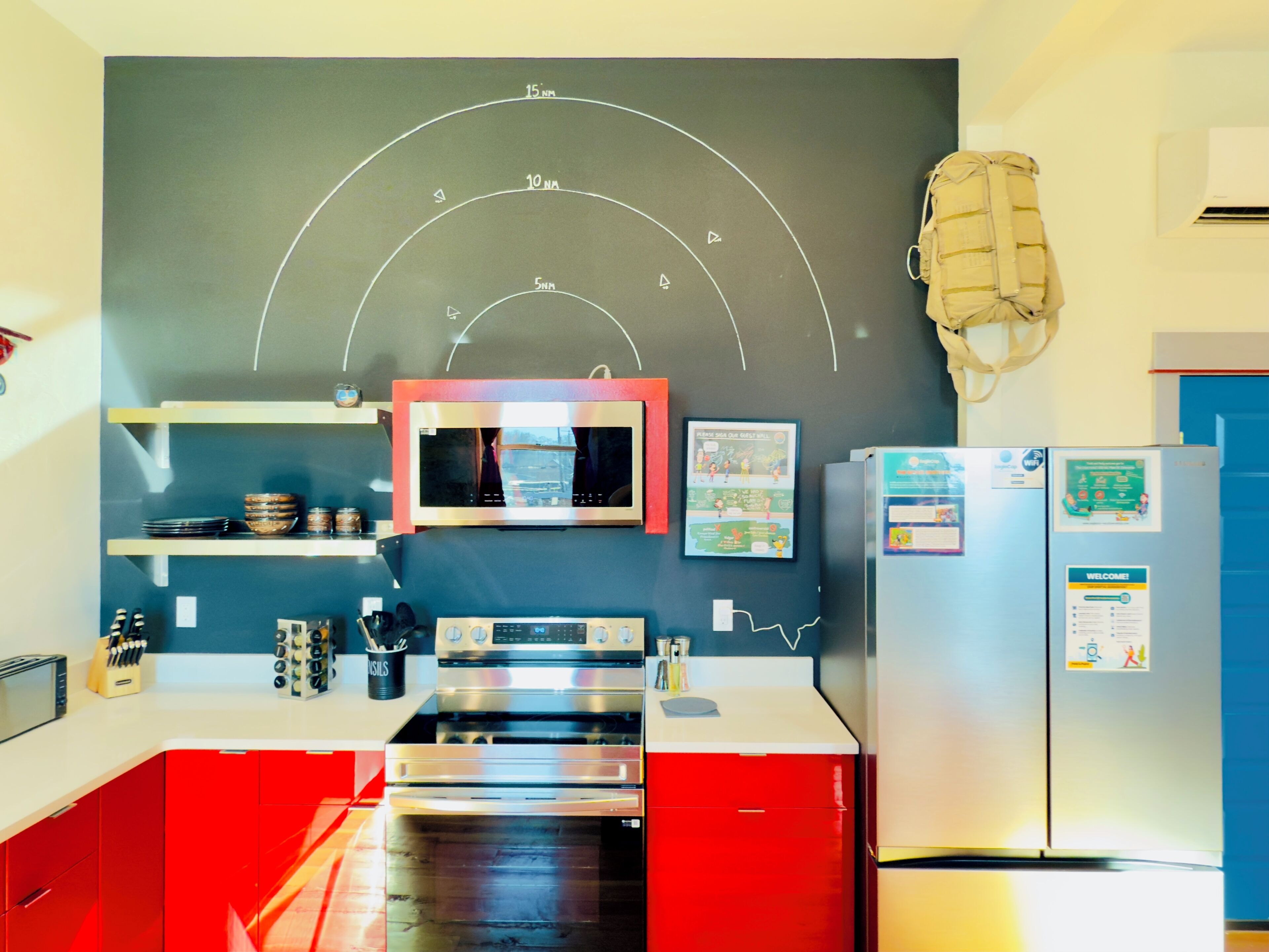 A kitchen with red cabinets, a microwave, a stove, and a refrigerator. There is a chalkboard with writing on the wall.