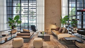 A modern living room with large windows, a sofa set, ottomans, a coffee table, and a bookshelf. - NEW Stunning 2/2 with Panoramic Views of Miami PH Condo 50th floor (Miami)