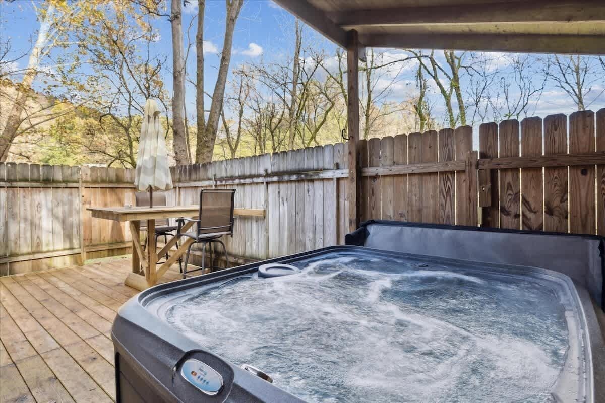 Un bain à remous installé sur une terrasse en bois, agrémentée d’une clôture en bois, d’une table et de chaises.