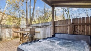 A hot tub in a wooden deck area with a wooden fence, a table, and chairs. - Stone Haven Retreat by Beyond Expectations: Dog Friendly w/ Hot Tub & Fireplace (Sevierville)
