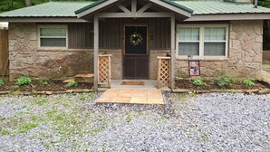A stone house with a green roof, a front porch, and a number '2502' above the door. - Stone Haven Retreat by Beyond Expectations: Dog Friendly w/ Hot Tub & Fireplace (Sevierville)