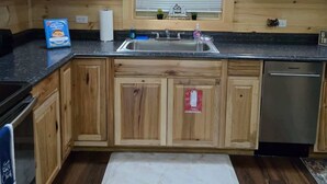 A kitchen with wooden cabinets, a stainless steel sink, a dishwasher, and a window with blinds. - Stone Haven Retreat by Beyond Expectations: Dog Friendly w/ Hot Tub & Fireplace (Sevierville)