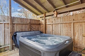 A hot tub under a wooden pergola with a wooden fence in the background.
