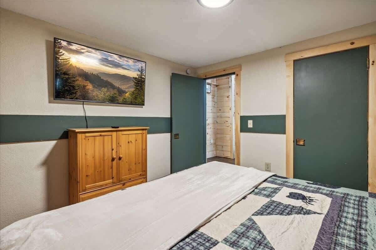 A bedroom with a bed, a wooden wardrobe, a painting on the wall, and a door.
