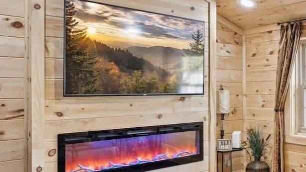 A wooden cabin interior with a fireplace, a mounted television, and a ceiling light fixture. - Stone Haven Retreat by Beyond Expectations: Dog Friendly w/ Hot Tub & Fireplace (Sevierville)