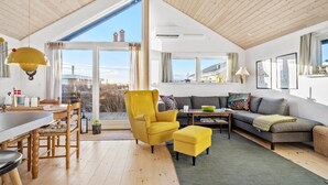 A spacious living area with a high ceiling, a dining area with a wooden table and chairs, a yellow armchair, a gray sofa, and a view of buildings through large windows. - Stunning home in Haderslev with WiFi (Haderslev)