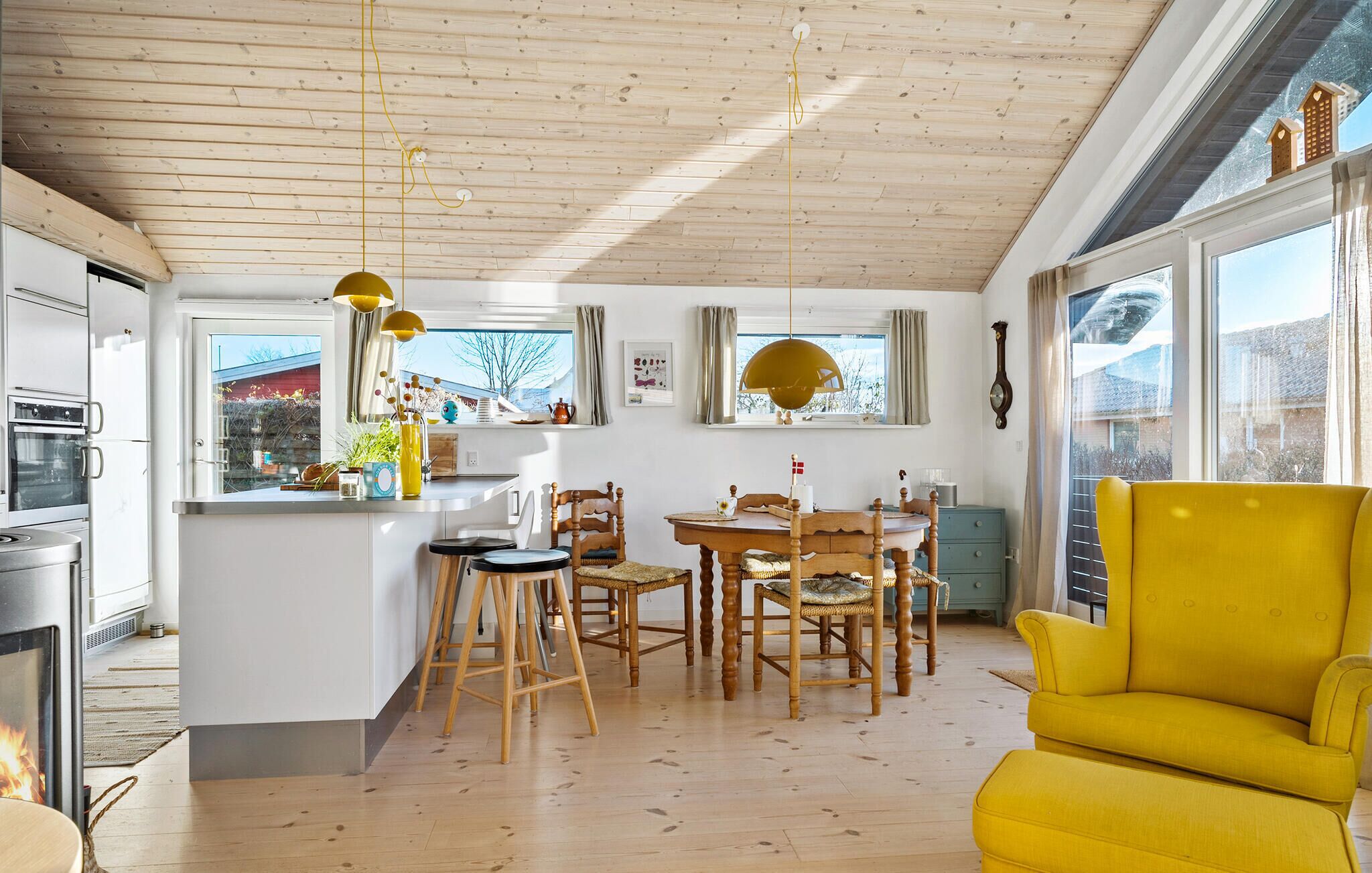 Una cocina moderna con armarios de madera, un comedor con sillas de madera y un sillón amarillo.