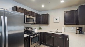 A modern kitchen with dark wooden cabinets, stainless steel appliances, a microwave, a toaster, and a coffee maker. - 6G Moab RedCliff Condo, POOL & HOT TUB (Moab)