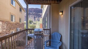 A balcony with a grill, a blue chair, and a view of mountains. - 6G Moab RedCliff Condo, POOL & HOT TUB (Moab)