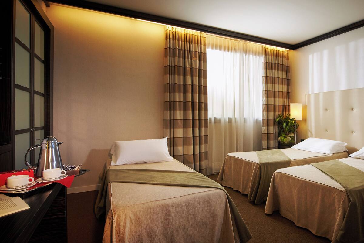 Une chambre d’hôtel avec deux lits, un bureau avec une machine à café et une fenêtre avec des rideaux.