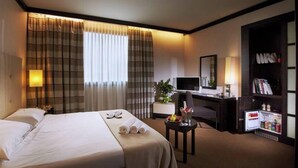 A hotel room with a bed, a desk, a chair, a TV, a bookshelf, and a minibar. - Hotel PisaValdera (Pontedera)