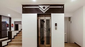 An elevator entrance with a modern design, a fire extinguisher on the wall, and a staircase leading to another floor. - The Onyx (Nagpur)