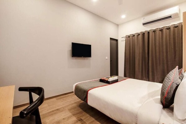 Une chambre d’hôtel avec un lit, un téléviseur fixé au mur, une chaise et un rideau.