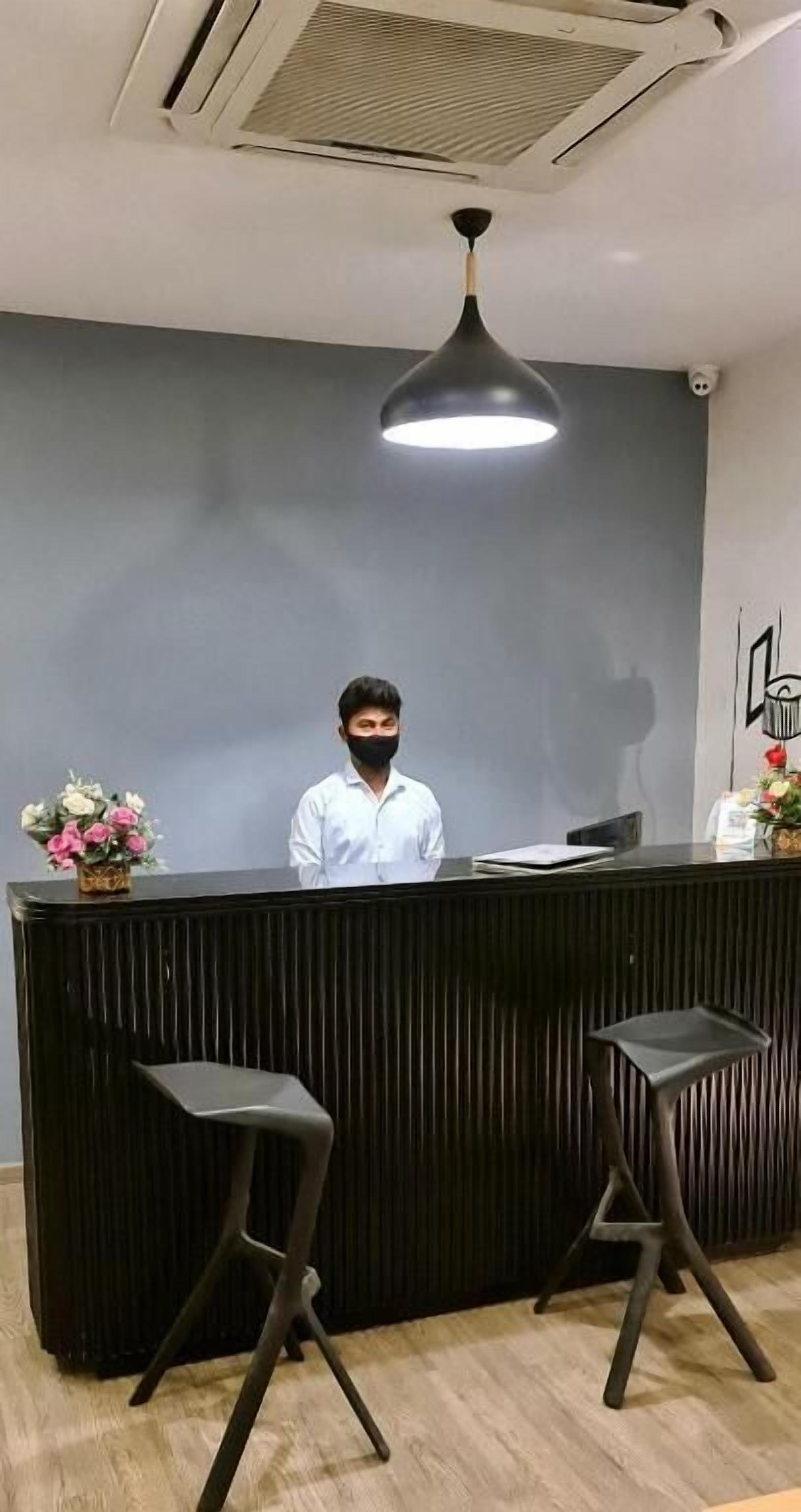 Una recepción con diseño moderno, dos taburetes negros, un florero y una lámpara del techo.