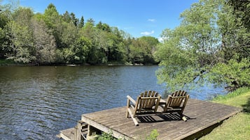 Eine hölzerne Anlegestelle mit zwei Stühlen, die auf einen stillen See mit umgebender Baumlandschaft blicken.
