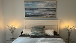 Ein Schlafzimmer mit einem großen Bett, einem Kopfteil, einem Bild über dem Bett und zwei Nachttischen mit dekorativer Beleuchtung.