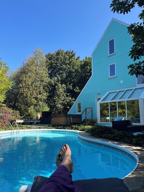 Una piscina amb una persona relaxant-se a la vora, un hivernacle i un edifici de dues plantes amb finestres.
