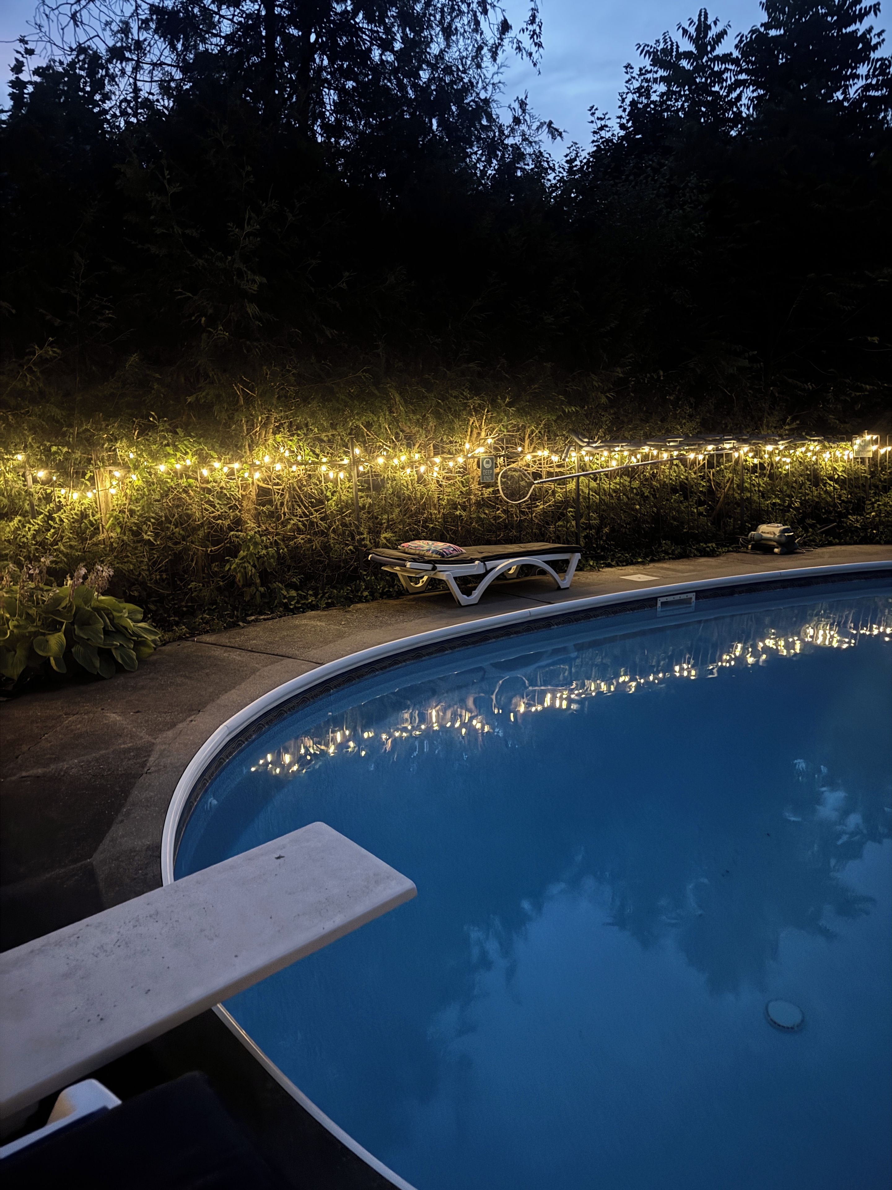 A swimming pool with a bench and string lights along the edge.