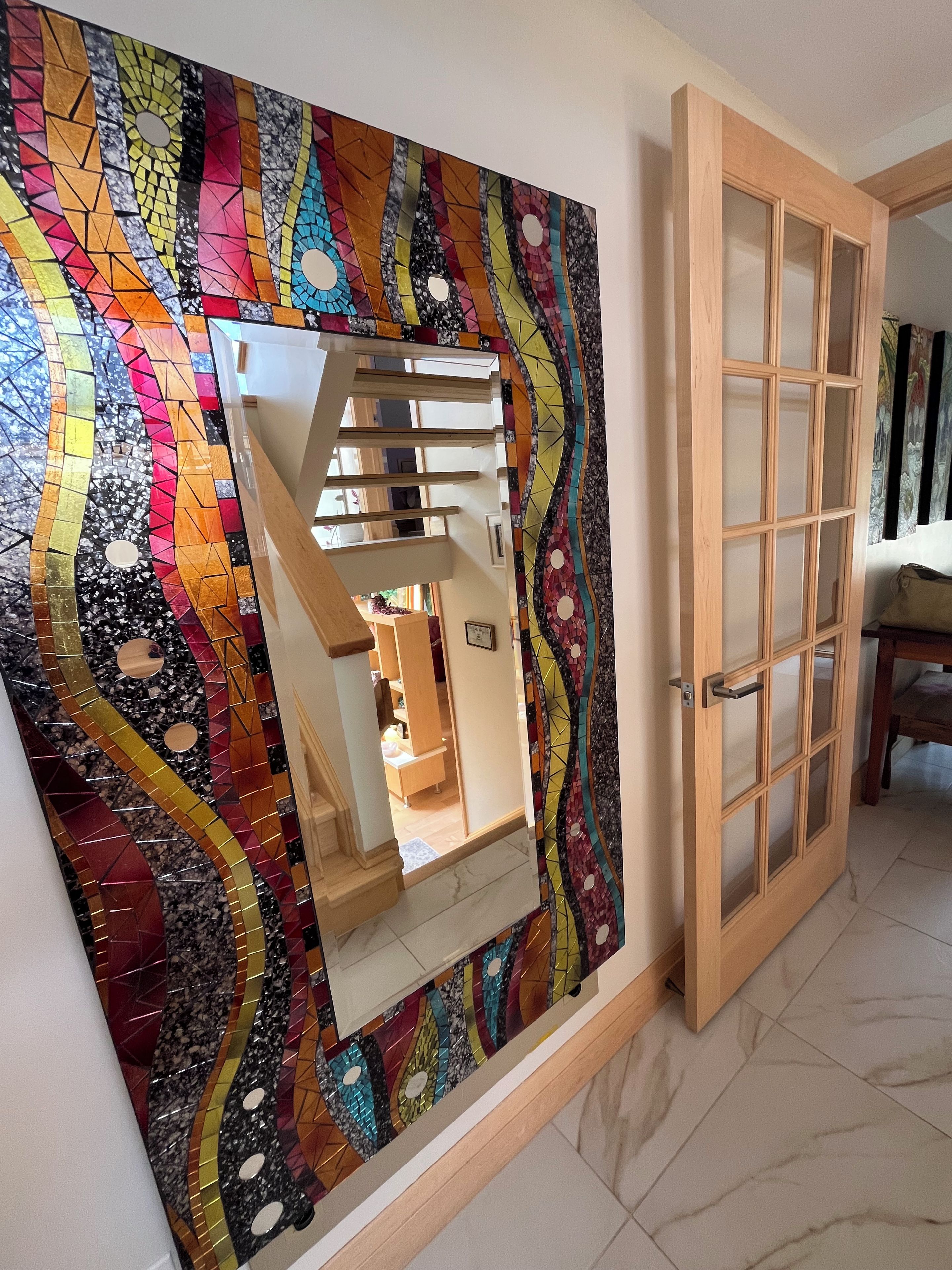 A staircase with a colorful mosaic wall and a wooden door with glass panels.