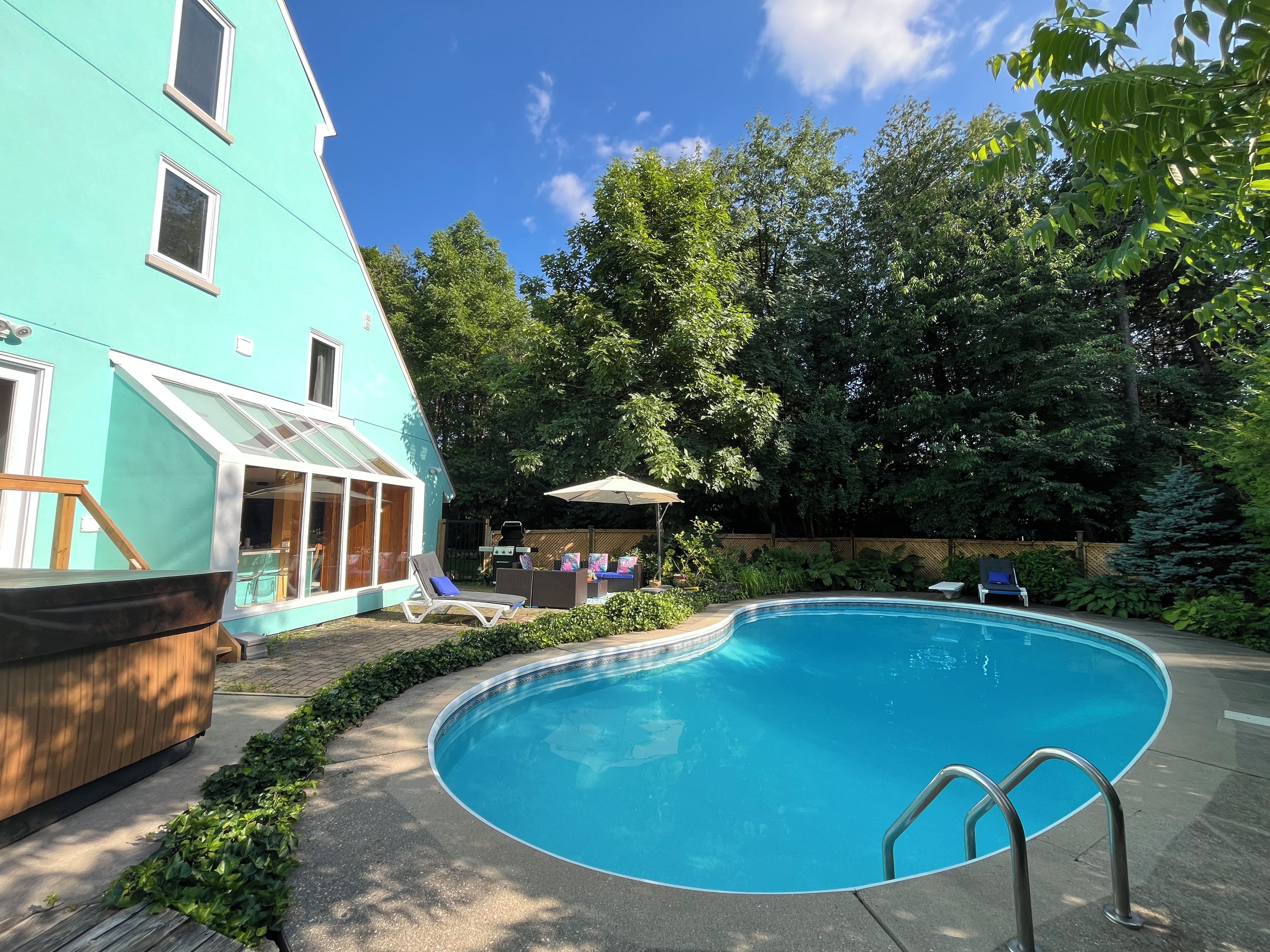 Ein Swimmingpool mit Metallleiter, umgeben von Grünpflanzen und einem Gebäude mit großen Fenstern.