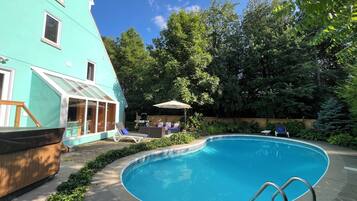 Ein Swimmingpool mit Metallleiter, umgeben von Grünpflanzen und einem Gebäude mit großen Fenstern.