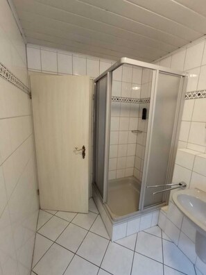 Et badeværelse med hvide flisegulve og vægge, en bruseniche og en vask.