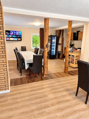 A dining area with a table and chairs, a television mounted on the wall, and a refrigerator.