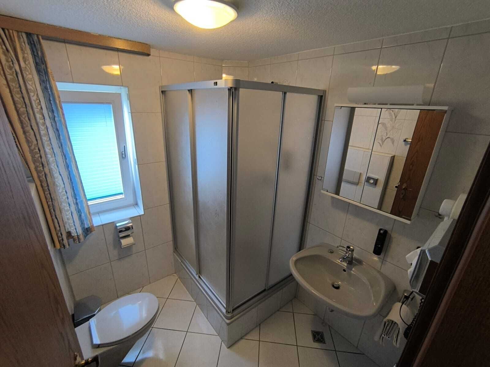 A bathroom with a shower, toilet, sink, and a window with curtains.