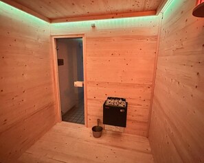 A wooden sauna room with a door, a bucket, and a box of wood pellets. - Comfortable and versatile room-perfect for relaxation, work and exchange (Winterberg)