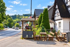 Um café à beira da estrada com mesas ao ar livre, uma motocicleta estacionada e uma estrada com carros ao fundo.