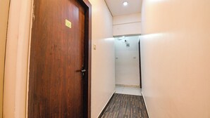 A narrow hallway with a wooden door marked with the number 105, leading to a room with a white ceiling and a visible electrical outlet. - Hotel Green Leaf (Kolkata)