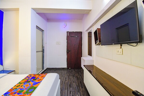 A narrow hotel hallway with a bed, a TV mounted on the wall, and a door at the end.