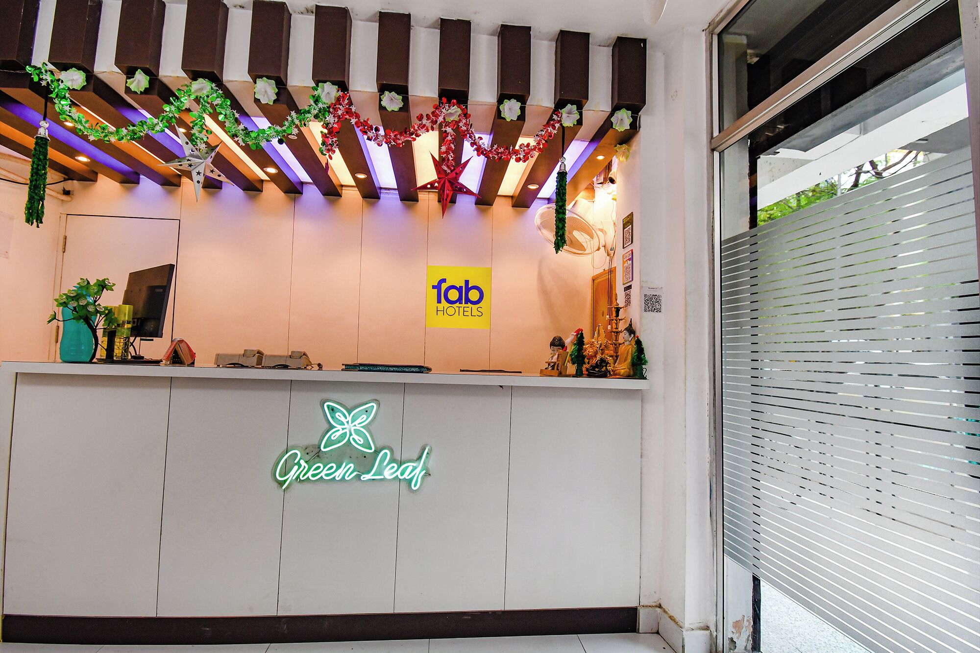 Bancada de recepção de hotel com um letreiro de neon que diz "Green Leaf" e uma placa para "fab hotels".