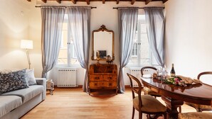 Een kamer met een houten plafond, een bank, een dressoir, een spiegel, een eettafel met stoelen en gordijnen.