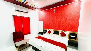A hotel room with a bed, a red chair, a bedside table, and a red patterned wall. - Hotel Amar Haveli (Jaisalmer)
