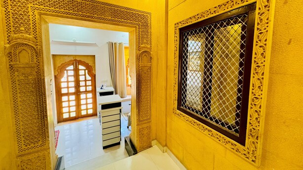 A hallway with ornate architectural details, a tiled floor, and a window with a decorative grille. - Hotel Amar Haveli (Jaisalmer)