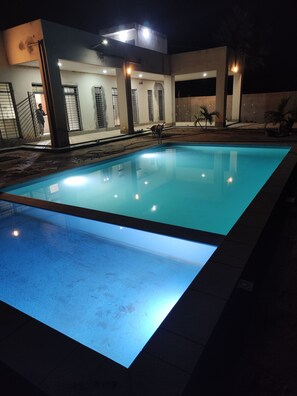 Une piscine à l’eau d’un bleu limpide, entourée d’un bâtiment doté de nombreuses fenêtres et d’un escalier menant à un niveau supérieur.