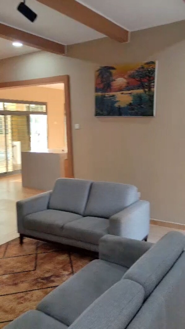 Un salon avec un canapé gris, un tableau au mur et une vue sur l’extérieur.
