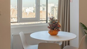 Una habitación moderna con una mesa redonda y dos sillas, una ventana con vistas a edificios y un radiador.