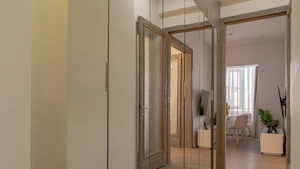 Un pasillo con pared espejada, piso de madera y una puerta que da a otra habitación.