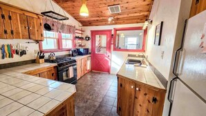 Une cuisine avec des meubles de rangement en bois, une porte rouge et un sol carrelé.