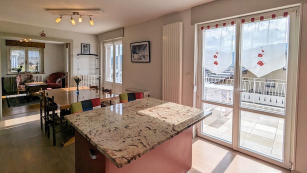 A spacious kitchen with a granite countertop, a dining area with a table and chairs, and large sliding glass doors leading to a balcony.