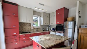 A modern kitchen with red and white cabinets, a granite countertop, stainless steel appliances, and a window providing natural light.