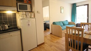 A compact kitchen with a microwave, coffee maker, and a refrigerator. There is a dining area with a table and chairs, and a sofa in the adjacent living space.