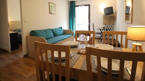A compact living space with a sofa, dining table, chairs, a TV, and a lamp.