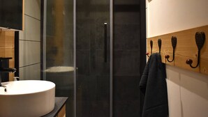 Een moderne badkamer met een douchecabine van glas, een witte wastafel en houten handdoekhaakjes aan de muur.